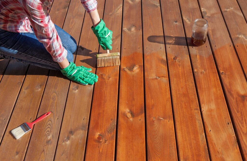 person with green gloves painting wooden deck floor boards