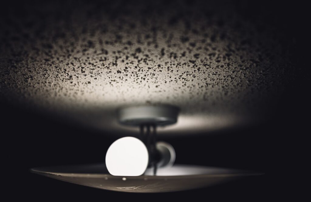 Aged look of popcorn textured white ceiling and a dual light fixture and glass cover | does popcorn ceiling have asbestos