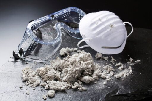 safety goggles, face mask, and asbestos on a dark surface