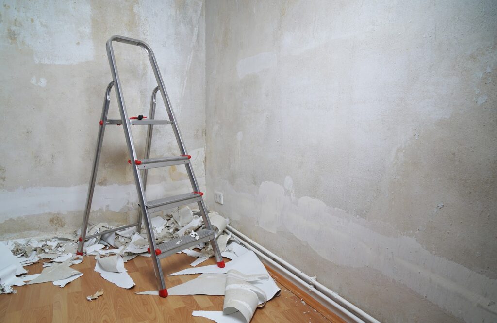 A ladder, near a wall stripped off of old wallpaper