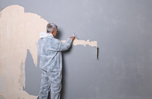 Man in overalls removing old wallpaper from the wall. | professional wall removal